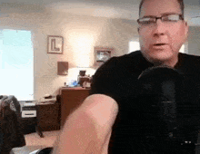a man wearing glasses and a black shirt is talking into a microphone .