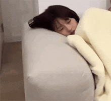 a woman is sleeping on a white couch with a blanket on it .