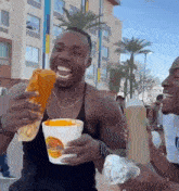 a man in a black tank top is holding a cup of food in his hand