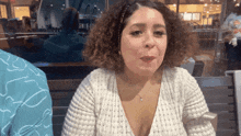 a woman with curly hair is wearing a white shirt and necklace