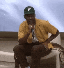 a man wearing a green f hat is sitting in a chair holding a microphone