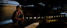 a man in a spiderman costume is sitting on a ledge in a dark room .