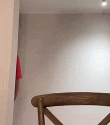 a person in a red shirt is standing behind a wooden chair in front of a white wall .