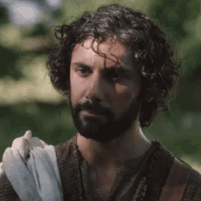 a man with curly hair and a beard is wearing a brown sweater