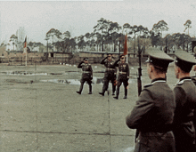 a group of men in military uniforms salute in a field with trees in the background