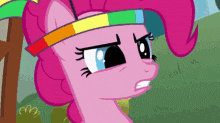 a pink pony wearing a rainbow headband looks angry