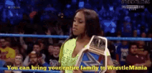 a woman in a wrestling ring holds a championship belt and says you can bring your entire family to wrestlemania
