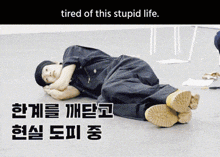a man is laying on the floor with the words tired of this stupid life above him