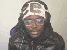 a man wearing glasses , headphones and a hat is looking at the camera .