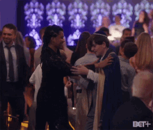 a woman is hugging a man in a crowd of people with the bet logo in the corner