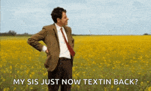 a man in a suit and tie is standing in a field of yellow flowers with his hands on his hips .