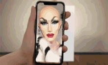 a person is holding a phone with a drag queen on the screen