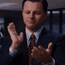 the man is wearing a suit and tie and clapping his hands .