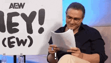 a man is sitting in front of a sign that says `` hey ! '' and reading a piece of paper .