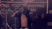 a shirtless man is singing into a microphone in front of a sign that says bbc
