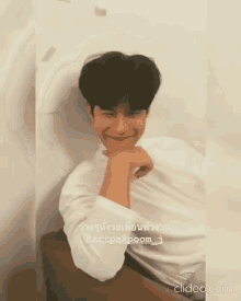 a man in a white shirt is sitting down with his hand on his chin and smiling .