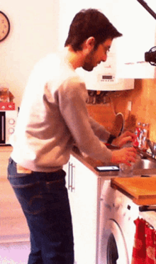 a man in a kitchen with a clock on the wall above him