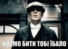 a man in a suit and hat is standing in front of a sign that says " idemo biti tobi ibalo "