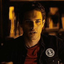 a man wearing a black jacket and a red shirt has a patch on his jacket that says ' karate ' on it .