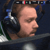 a man wearing headphones and a microphone looks at a monitor with a scoreboard that says planted