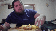 a man in a blue shirt is sitting at a table eating fried food