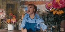 a woman is sitting at a table with a vase of flowers and a pitcher of wine .