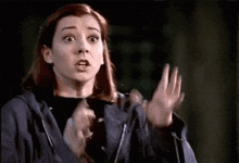 a woman in a blue jacket is making a surprised face while holding her hands up in the air .