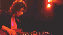 a man playing a guitar in a dark room with red lights behind him