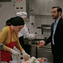 a man in a suit stands next to a woman in a red apron cutting vegetables