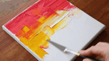 a person is painting on a canvas with yellow and red paint