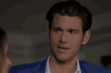 a man in a blue suit and white shirt is talking to a woman and making a funny face .