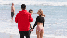 a man in a red hoodie is walking on the beach
