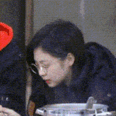 a woman wearing glasses is sitting at a table with a pot of food in front of her .