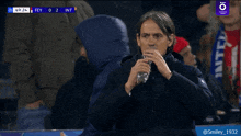 a man drinks water from a bottle while watching a soccer game