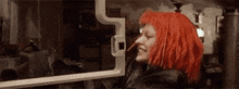 a woman with red hair is standing in front of a window and smiling .
