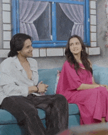 a man and a woman are sitting on a blue couch in front of a window
