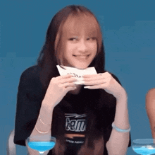 a girl is holding a piece of paper in her hands and smiling while sitting at a table with two glasses of water .