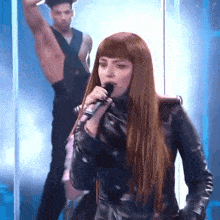 a woman singing into a microphone while a man stands behind her