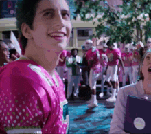 a man wearing a pink shirt with white polka dots smiles in front of a crowd