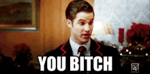 a man in a suit and tie is making a funny face and saying you bitch .