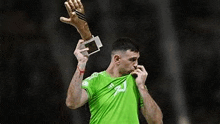 a soccer player in a green shirt is holding a trophy and a glove .