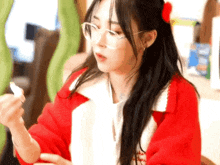 a woman wearing glasses and a red jacket is sitting at a table holding something in her hand .