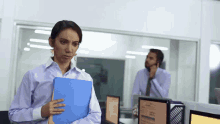 a woman holding a blue folder in front of a man on a phone