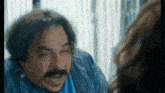 a man with a mustache is making a funny face while looking at a woman .