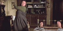 a woman in a green dress is holding a wooden stick over a man laying on a bed
