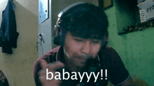a man wearing headphones says babayyy !! in front of a green wall