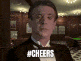 a man in a tuxedo says cheers in a room