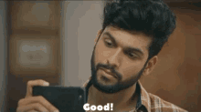 a man with a beard is taking a picture of himself with a cell phone and the word good is above him