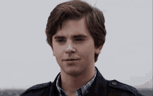 a young man wearing a plaid shirt and a jacket is looking at the camera