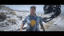 a man in a shirt with a golden state warriors logo on it is walking in the desert with a monster behind him .